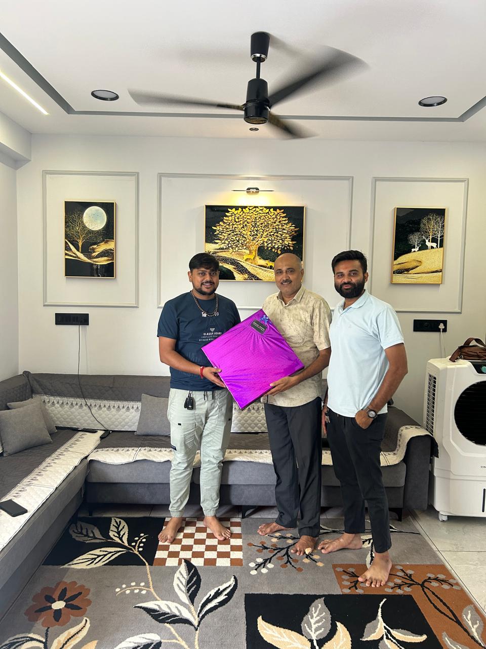 Sarvamangal team with a client holding a purple-wrapped gift in a living room